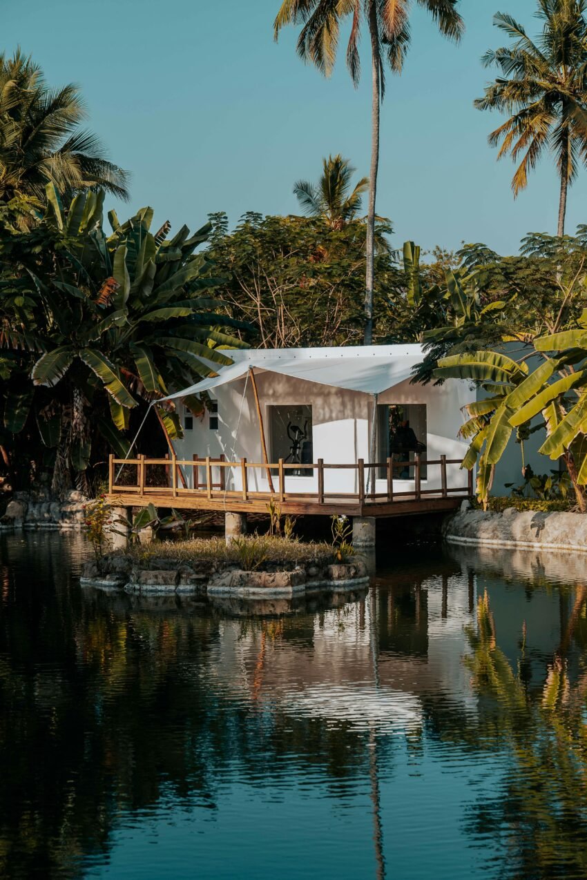 Serene lakeside tent surrounded by lush tropical vegetation and palm trees.