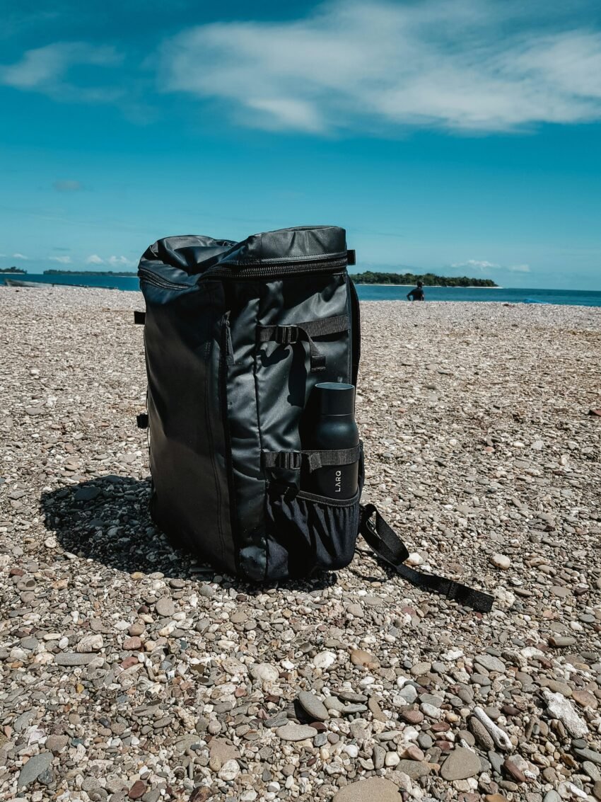 A durable gym bag for men sitting on the pavement against a clear blue sky backdrop.